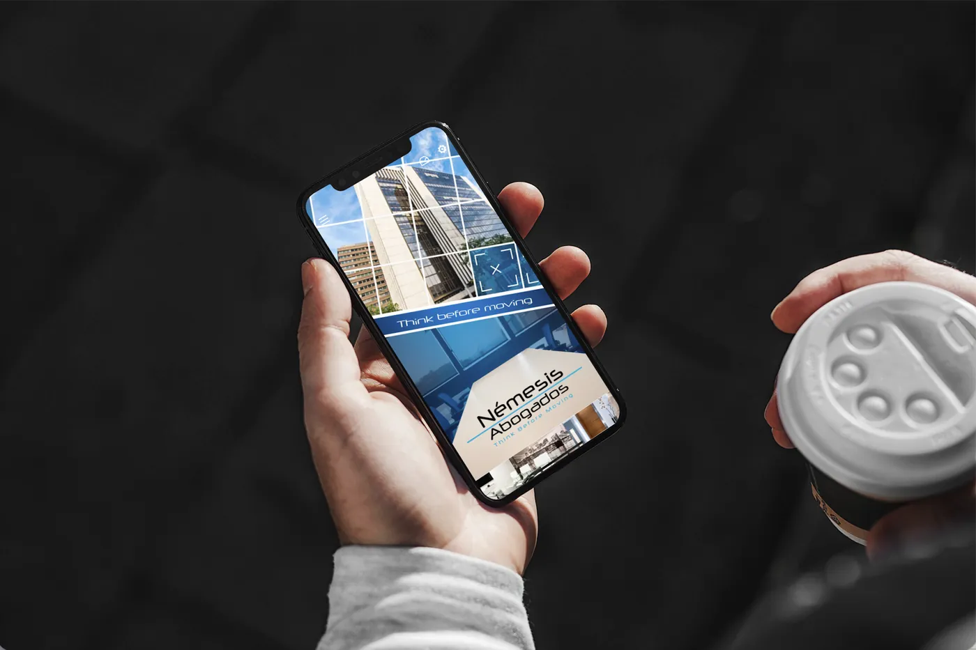 App móvil de Némesis Abogados creada con Scoreapps, sostenida en la mano con un café.